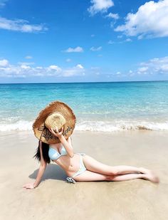 Woman in a light blue bikini lying on a sandy beach with a straw hat covering her face