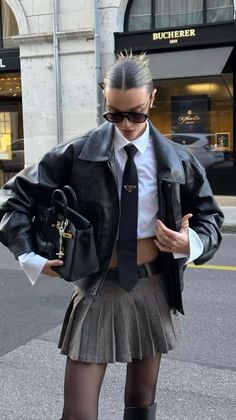 Woman in a leather jacket, crop top, and pleated mini skirt on a city street