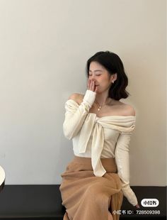 Woman in an off-shoulder top and brown skirt, covering her mouth with her hand
