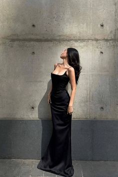 Woman in a black slip dress posing against a concrete wall