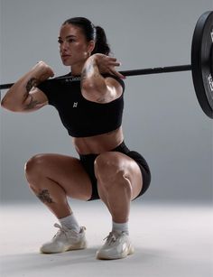 Muscular woman squatting with a barbell in a studio setting