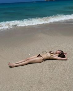 Woman in a bikini lying on a sandy beach with waves in the background