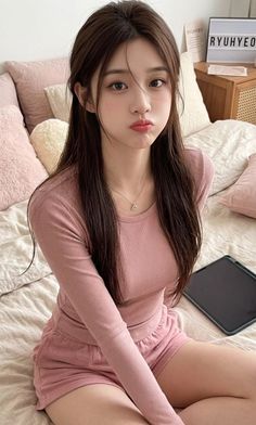 Woman with long hair in a pink top and shorts sitting on a bed