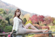 Woman in a tight dress and cardigan sitting on a wooden fence outdoors