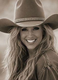 Woman in a cowboy hat and denim jacket smiling in a sepia-toned portrait