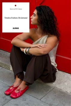 Woman with curly hair sitting on a sidewalk against a red background