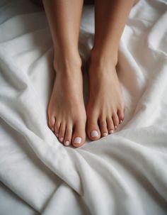 Pair of feet with white nail polish on white sheets