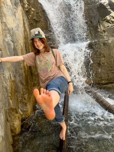 Person in a t-shirt and jeans posing barefoot by a waterfall