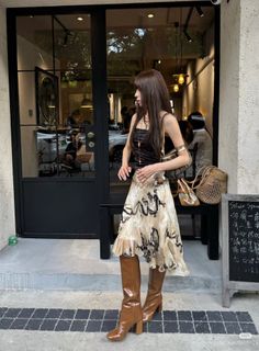Woman in a strapless top, midi skirt, and brown boots standing outside a cafe