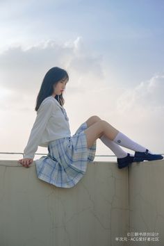 Woman in a school uniform sitting on a wall outdoors under a cloudy sky