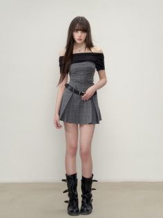 Woman in an off-shoulder top and plaid skirt with black boots standing indoors