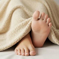 Feet peeking out from under a soft blanket with light pink nail polish
