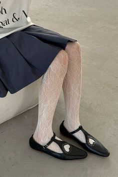 Person wearing white lace tights, a pleated skirt, and black mary jane shoes