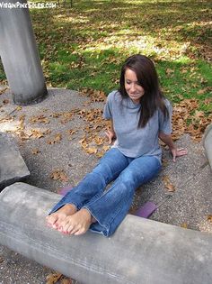 Woman with long hair and blue jeans sitting outdoors with bare feet