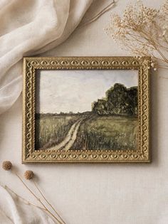Watercolor painting of a country road through a grassy field in a gold frame