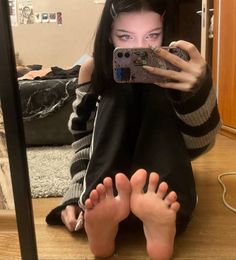Woman in a striped sweater and black pants taking a mirror selfie, showing her feet