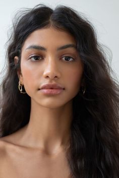 Woman with long wavy hair and gold hoop earrings looking directly at the camera