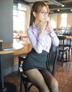 Woman in a light purple shirt and black mini skirt sitting indoors