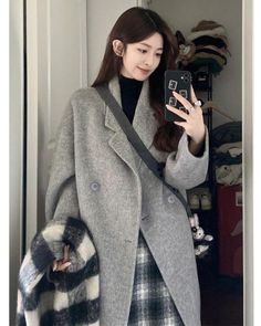 Woman in a gray coat and plaid skirt taking a mirror selfie indoors