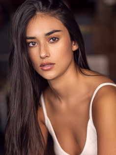 Woman with long dark hair and freckles wearing a white top, looking at the camera