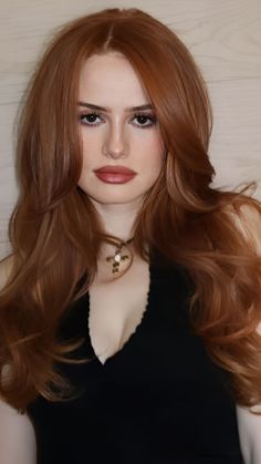 Woman with long red hair and a black top with a cross necklace