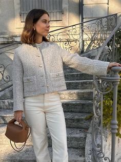 Woman in a tweed jacket and white pants holding a brown handbag on outdoor stairs