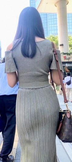 Woman with long dark hair wearing an off-shoulder top and pleated skirt outdoors