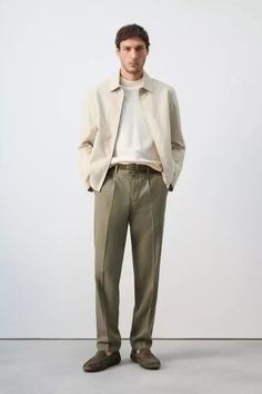 Man in a beige jacket, turtleneck, and khaki pants standing in a studio