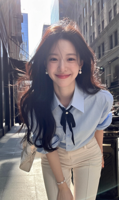 Woman with long dark hair and a light blue shirt smiling on a city street