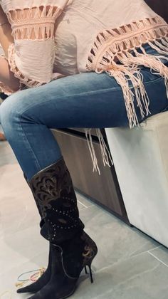 Person wearing blue jeans, a fringe top, and high heel boots indoors