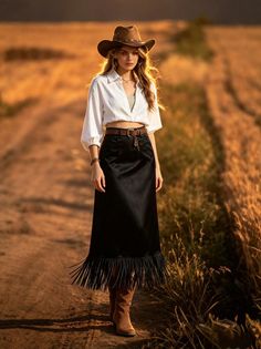 Woman in a cowboy hat and black skirt walking on a dirt path at golden hour