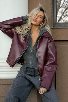 Woman with blonde hair in a leather jacket and gray sweater posing outdoors