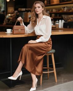 Woman with long wavy hair in a white blouse and brown skirt sitting in a cafe