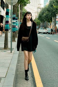 Woman with long black hair walking on a city street during the day
