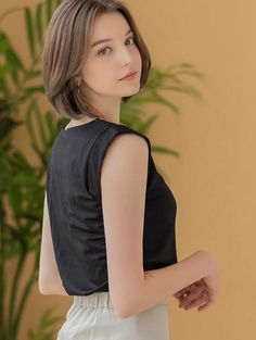 Woman with short hair wearing a black top and light pants indoors