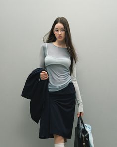 Woman with long hair and glasses wearing a sheer top and dark skirt