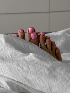 Feet with pink nail polish peeking out from under white sheets