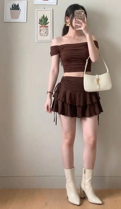 Woman in a brown off-shoulder top and ruffle skirt with white boots and handbag