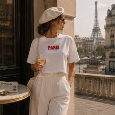 Woman in a white beret and outfit holding a wine glass with the Eiffel Tower in the background
