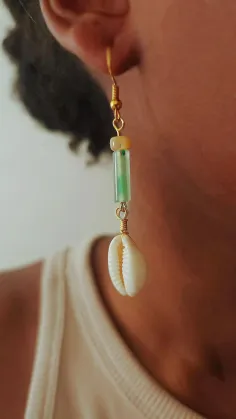 Close up of an ear with a dangle earring featuring a cowrie shell and green bead