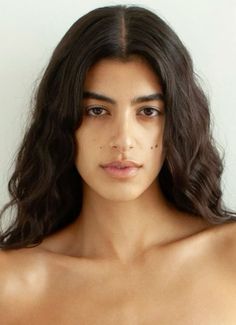 Woman with long dark wavy hair and bare shoulders looking directly at the camera