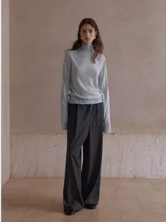 Woman in a light blue turtleneck and dark wide-leg pants indoors