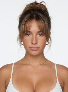 Woman with a messy bun and freckles wearing a white top and gold jewelry