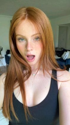 Woman with long red hair and green eyes wearing a black tank top indoors