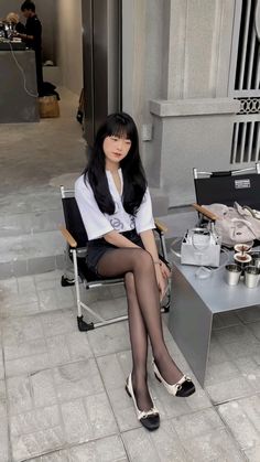 Woman with long black hair sitting outdoors in a white shirt and black shorts