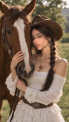 Woman in a white dress and cowgirl hat with a horse outdoors