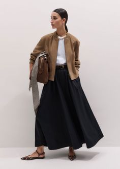 Woman in a brown bomber jacket and black maxi skirt holding a brown handbag