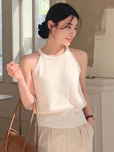 Woman with black hair in an updo wearing a white top and beige pants indoors