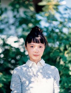 Woman with a bun and bangs wearing a sweater over a collared shirt outdoors