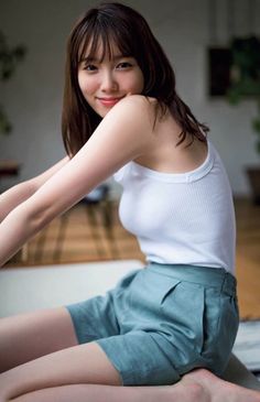 Woman in a white tank top and green shorts smiling indoors